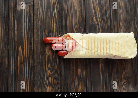 Salsiccia affumicata in pane pita al buio su un sfondo di legno.photo w Foto Stock