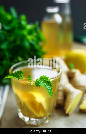 Vetro con lo zenzero detox di acqua ed altri ingredienti nelle vicinanze. Sfondo di legno. Foto Stock