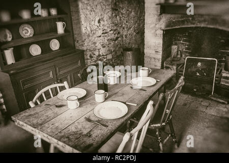 Poveri contadini interni dal xix secolo, la sala da pranzo con tavolo in legno e camino, seppia fotografia di stile Foto Stock