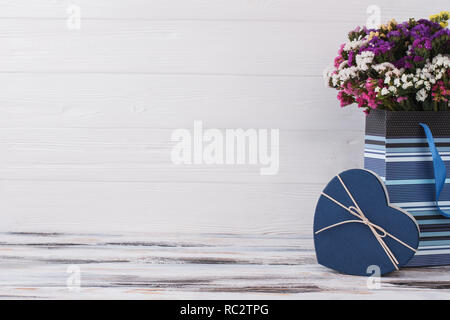 Fiori multicolori in borsa blu e spazio libero per il testo. Forma blu Scatola cuore dono. Presenta per il giorno di san valentino, copyspace bianco sullo sfondo di legno. Foto Stock