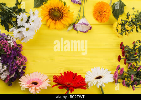 Diversi bellissimi fiori disposti intorno e copyspace. Spazio libero per il testo. Legno giallo sfondo scrivania. Foto Stock