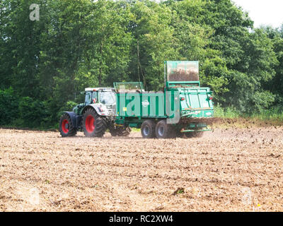 Agricoltore sul suo trattore accoppiato con una concimazione firtilizing rimorchio il suo acro vicino Barum, Elbmarsch, Bassa Sassonia, Germania. Foto Stock