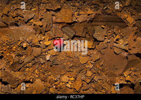 Piccolo rosso cuore di vetro sulla superficie secca di metallo arrugginito. Foto Stock