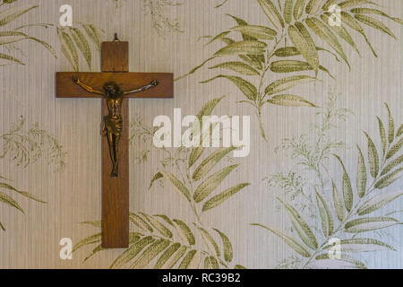 Croce di legno con un Gesù crocifisso scultura appeso a una parete, sfondo religioso Foto Stock