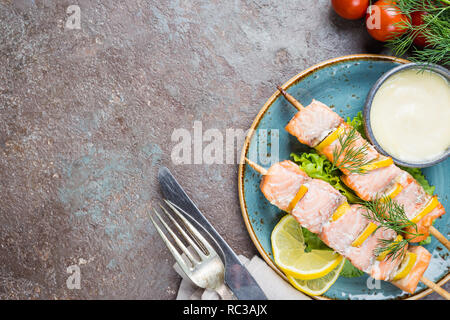 Grigliata di spiedini di salmone con limone e salsa di pietra scura sullo sfondo, vista dall'alto con spazio di copia Foto Stock