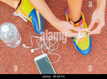 Sport runner donna lacci delle scarpe di legatura. La donna la sua legatura sneakers su uno stadio via di corsa. Il concetto di allenamento Foto Stock