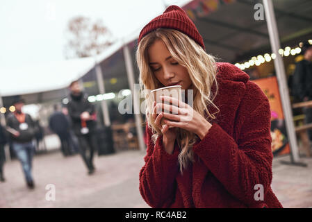 Bevanda calda in autunno. Close-up di donna bevendo un vin brulé presso la fiera mercato. La stagione fredda. Close-up foto di donna bionda Foto Stock