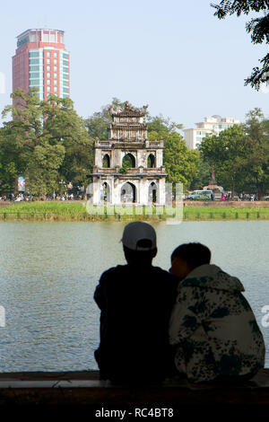 Vietnamita sfocati giovane seduta dal lago Hoan Kiem ad Hanoi, in Vietnam, in una giornata di sole. Incentrato sul vecchio tartaruga (Tartaruga) Torre. Foto Stock