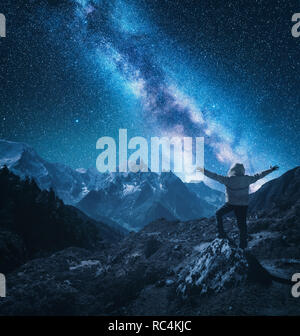 Silhouette di un uomo in piedi con sollevata bracci sulla pietra, montagne e il cielo stellato con via lattea di notte in Nepal. Stelle luminose. Viaggio. landsc Foto Stock