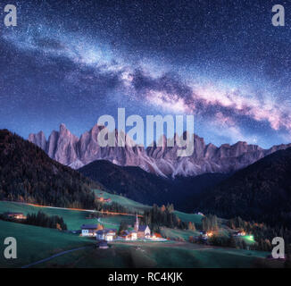 Santa Maddalena e via lattea di notte in autunno in Italia. Cielo stellato con via lattea oltre a Santa Maddalena e le montagne. Villaggio con case, chiesa, gr Foto Stock