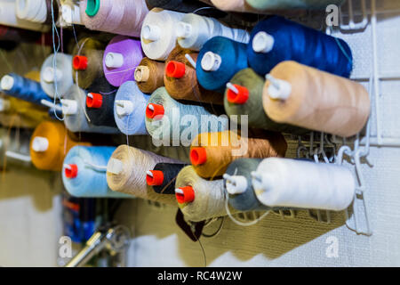 Coni colorati e rocchetti di filato in un atelier.sartoria, abbigliamento, designer workshop concetto. ricamo stelo thread.riga multicolore di bobine di filato, materiale di cucitura.luogo di lavoro del sarto Foto Stock