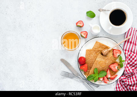 Crepes, frittelle sottili o blini con fragole, il miele, il caffè sul cemento dello sfondo. Vista superiore, copia spazio per il testo Foto Stock