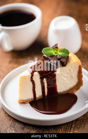 Cheesecake con salsa di cioccolato e la tazza di caffè nero con crema di latte su un tavolo di legno. Messa a fuoco selettiva Foto Stock