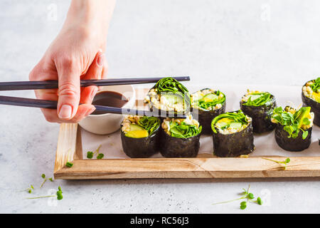 Vegan verde rotoli di sushi con avocado, germogli di cetriolo e nori su una tavola di legno e sfondo grigio. Foto Stock