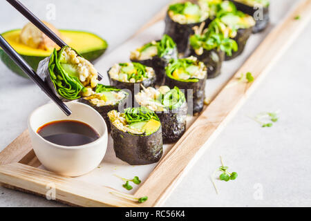 Vegan verde rotoli di sushi con avocado, germogli di cetriolo e nori su una tavola di legno e sfondo grigio. Foto Stock