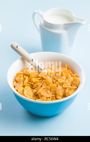 Cereali per la prima colazione o cornflakes nella ciotola e latte su sfondo blu. Foto Stock