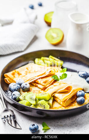 Sottile crepes con crema di ricotta, kiwi e mirtilli in una piastra nera. Cucina russa concetto. Foto Stock