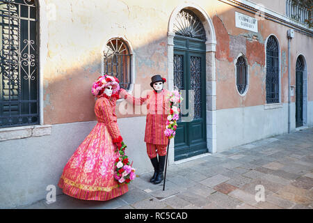 Venezia, Italia - 10 Febbraio 2018: matura in maschere bianche e rosse e gialle costumi floreali su strada durante il carnevale Foto Stock