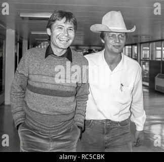 Paese americano cantante John Denver e attore David Soul che viaggiano attraverso l'aeroporto di Heathrow in rotta per Los Angeles, febbraio 1984. Foto Stock