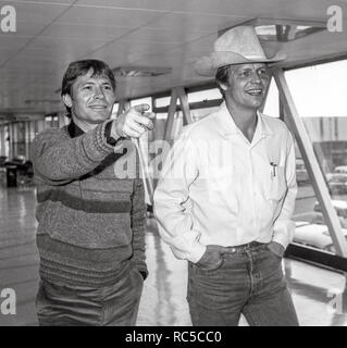 Paese americano cantante John Denver e attore David Soul che viaggiano attraverso l'aeroporto di Heathrow in rotta per Los Angeles, febbraio 1984. Foto Stock