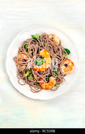 Soba, Tagliatelle di grano saraceno con gamberi e verdure, ripresa dall'alto su un pallido sfondo di legno con un posto per il testo Foto Stock