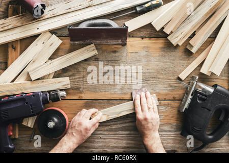 Carpenter lavorando nel laboratorio di falegnameria. Uomo di levigatura listone manualmente vista superiore Foto Stock