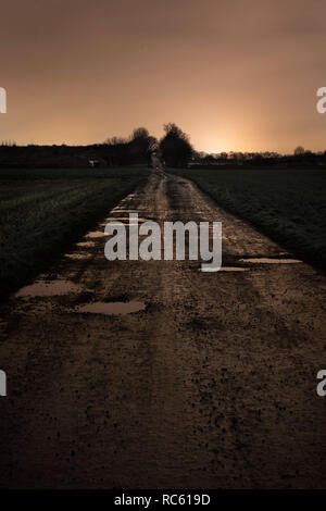 Un bagnato su strada sterrata con buche dopo il tramonto. Foto Stock