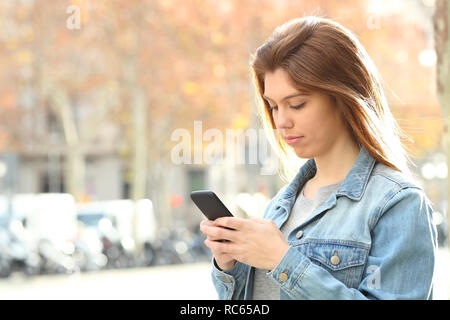 Grave ragazza adolescente chattare su smart phone a piedi in strada Foto Stock