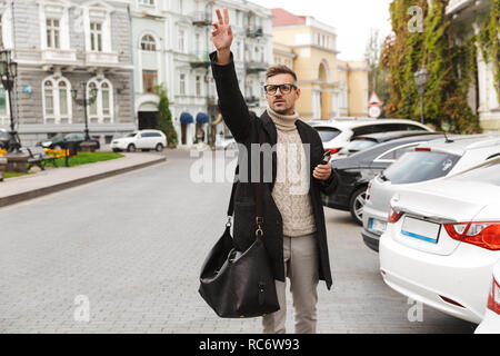 Uomo bello indossando un cappotto passeggiate all'aperto, la cattura di un taxi Foto Stock