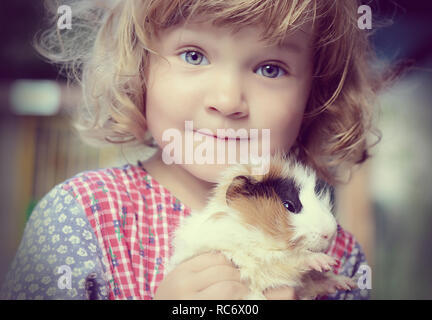 Carino toddler bianco ragazza in uno stile rustico abito rosso di contenimento cavia sulle mani Foto Stock