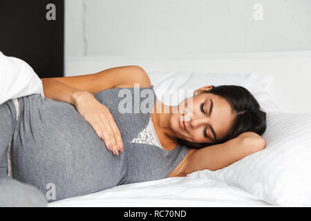 Immagine di un sano incredibile donna incinta al chiuso in casa risiede nel letto. Foto Stock