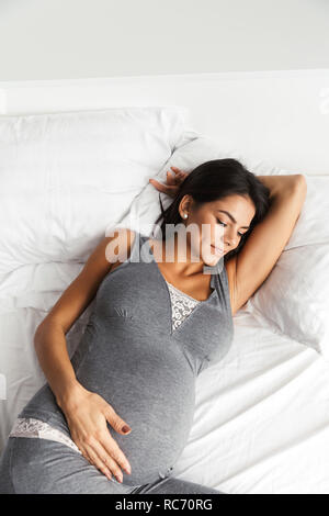 Immagine di un sano incredibile donna incinta al chiuso in casa risiede nel letto. Foto Stock