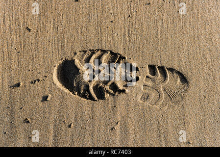Una sola impronta di un shoeprint in sabbia bagnata su una spiaggia. Foto Stock