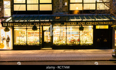 Vetrine decorate a Natale (illuminazione del marciapiede della strada, nome del baldacchino in vetro, sera d'inverno) - Bettys Café Tea Room, Ilkley, Yorkshire, Inghilterra, Regno Unito. Foto Stock