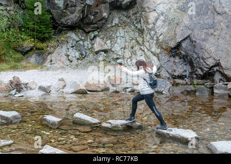 Donna salta su pietre miliari poste in un stagno. Fotografato sul 'Wild Water modo' Stubai, Tirolo, Austria Foto Stock