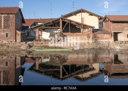 Vista sul verde vecchia barca ormeggiata davanti la casa tradizionale sul terrapieno artificiale della storica canal, girato in inverno una luce brillante a Bernate Ticino Foto Stock