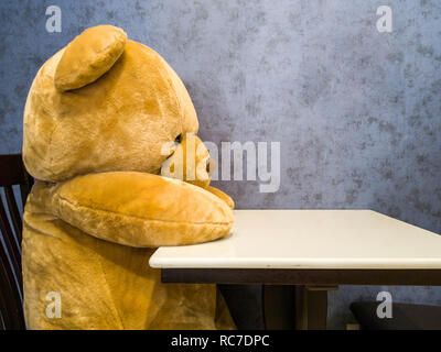 Simpatico orsacchiotto sedere sulla sedia davanti al tavolo da pranzo. Lo fanno sembrare in attesa di piatto preferito. Foto Stock