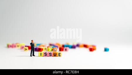 Figura in miniatura imprenditore in blu scuro tuta in piedi accanto al di colorati di rilascio alfabeto e pensare di modi per risolvere il problema. Foto Stock