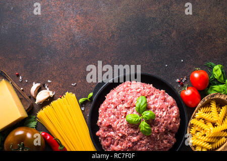 La carne macinata, la pasta e la verdura. Gli ingredienti per cucinare gli spaghetti alla bolognese. Vista superiore copia spazio su pietra scuro dello sfondo. Foto Stock