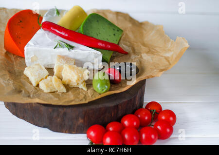 , Camembert Brie, il parmigiano reggiano, Formaggio verde con basilico e il peperoncino rosso formaggio giacciono su un bordo scuro accanto a pomodori, olive, aglio, noci e miele o Foto Stock
