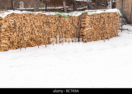 Tritate a secco di legna da ardere log memorizzati all'esterno. Tritate a secco i registri di legna da ardere pronto impilati in un giorno di neve. Foto Stock