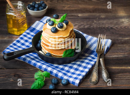Pila di Pancake fatti in casa nella padella di ferro con mirtilli, banana e foglie di menta sul legno rustico sfondo. Foto Stock