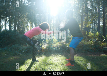 Voce maschile e femminile stretching gambe e il riscaldamento nella foresta soleggiato Foto Stock