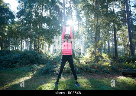 Runner bracci di stretching e riscaldamento nella foresta soleggiato Foto Stock