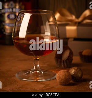 Un bicchiere di forte bevanda alcolica il brandy o il brandy e una scatola di cioccolatini su uno sfondo scuro. Messa a fuoco selettiva. Foto Stock