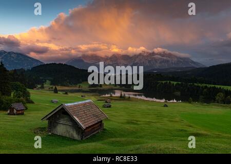 Piccola capanna sul prato di montagna con Geroldsee, sullo sfondo delle montagne Karwendel con drammatica cloud sky, Gerold, Mittenwald Foto Stock
