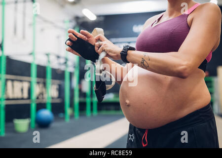 Donna incinta mettendo su guanti allenamento in palestra Foto Stock