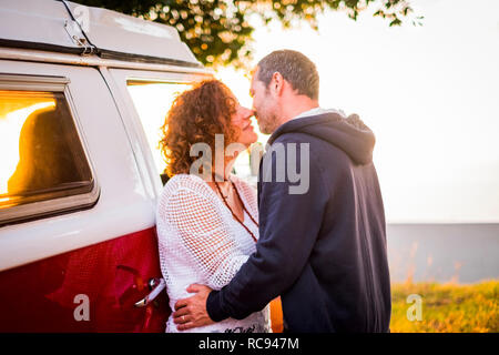 Giovane età media adulto uomo e donna baciare con amore all'aperto durante i viaggi vacanza - bus rosso in background e tempo al tramonto Foto Stock