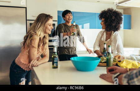 Sorridendo gli uomini e le donne a parlare e ridere mentre si beve birra in casa. Gli amici seduti al tavolo da pranzo con spuntini e bevande aventi fun. Foto Stock