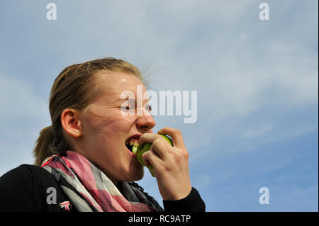 Junge Frau beisst in einen grünen Apfel - in den sauren Apfel beissen | giovane donna mangia una mela verde - per ingoiare una pillola amara o per afferrare il natt Foto Stock
